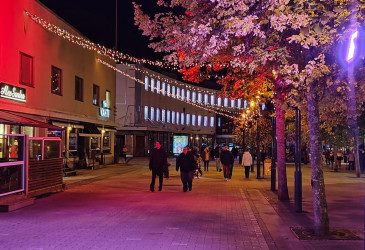 Kävelykatu Koskenparras iltavalaistuksessa punasävyisin valoin, ihmisiä kävelyllä.