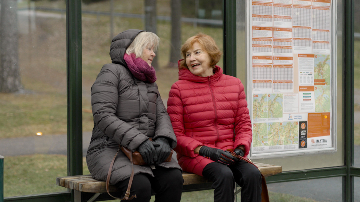 Kaksi vanhaa naista istumassa bussipysäkillä .