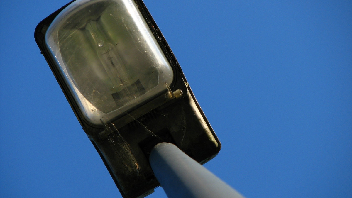 Уличный фонарь сфотографирован снизу на фоне голубого неба.