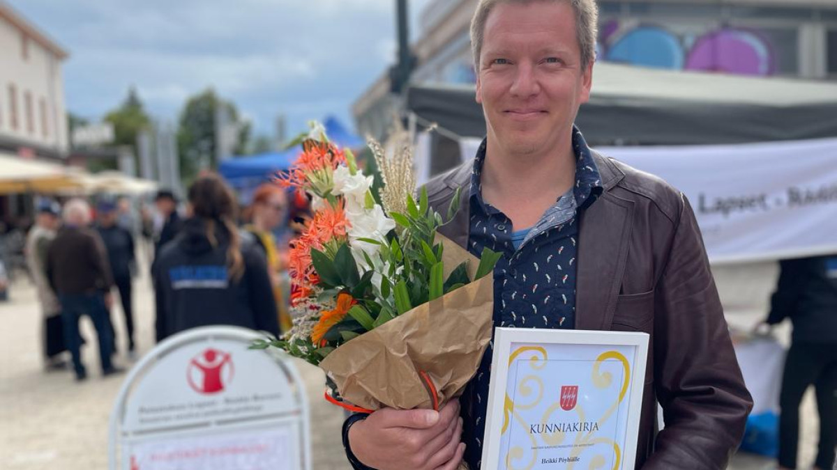 Heikki Pöyhia has flowers and an award certificate in his hands.
