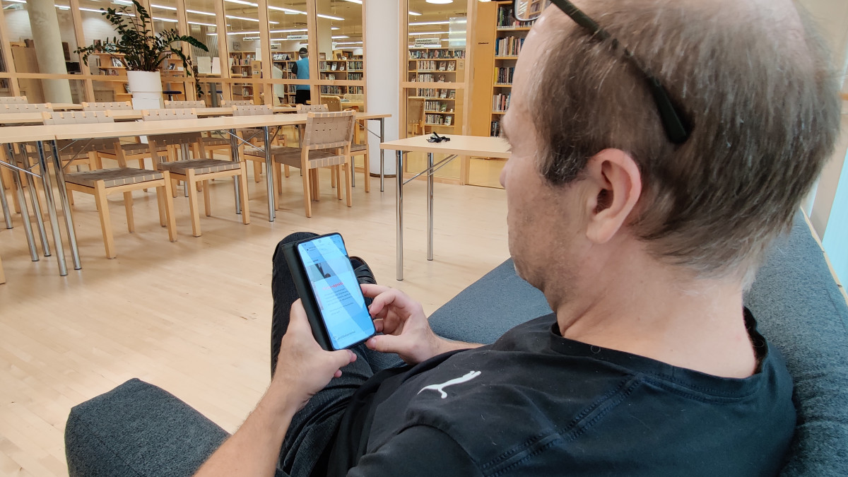 Мужчина смотрит в телефон на диване в библиотеке.