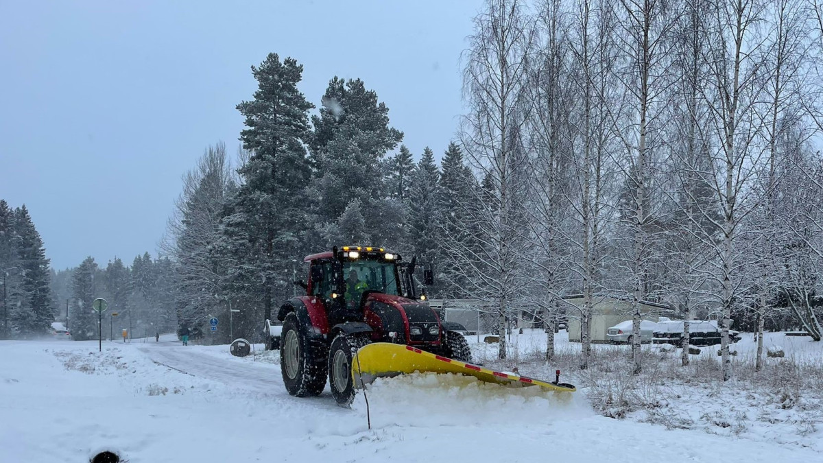 Traktori auraa jalkakäytävää lumisateessa.