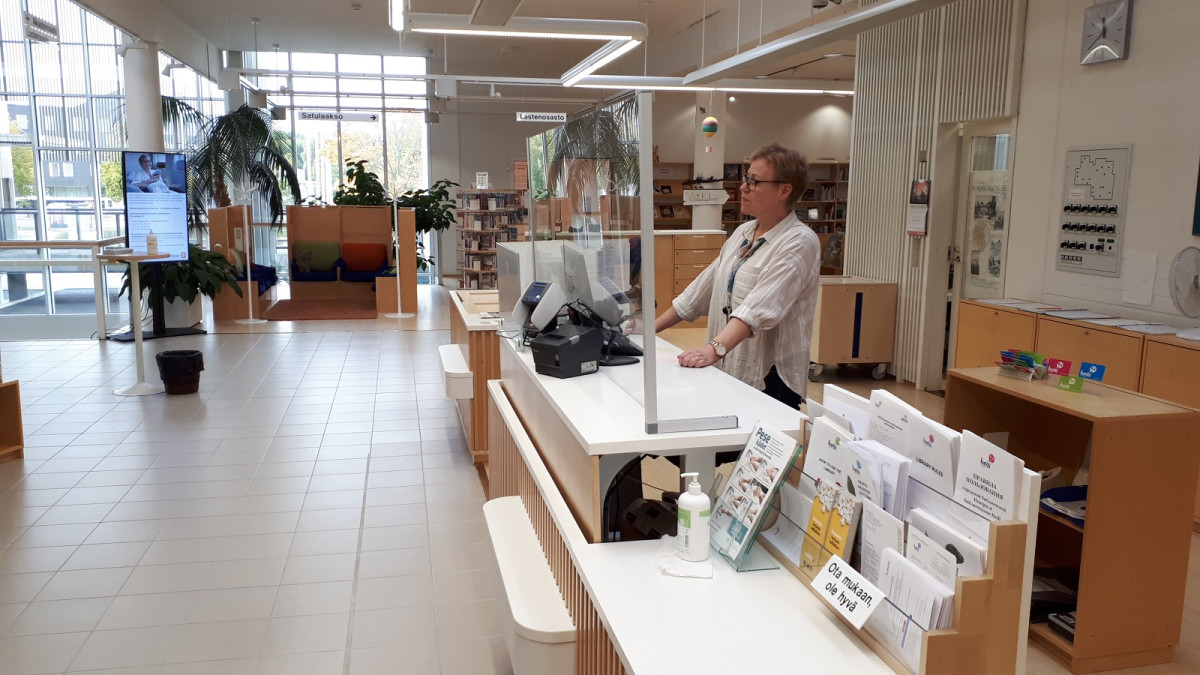 The librarian is standing behind the lending desk of the Imatra main library, photo from the side.