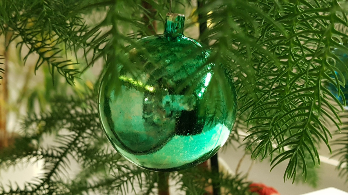 A green Christmas ball hangs on a fir branch.