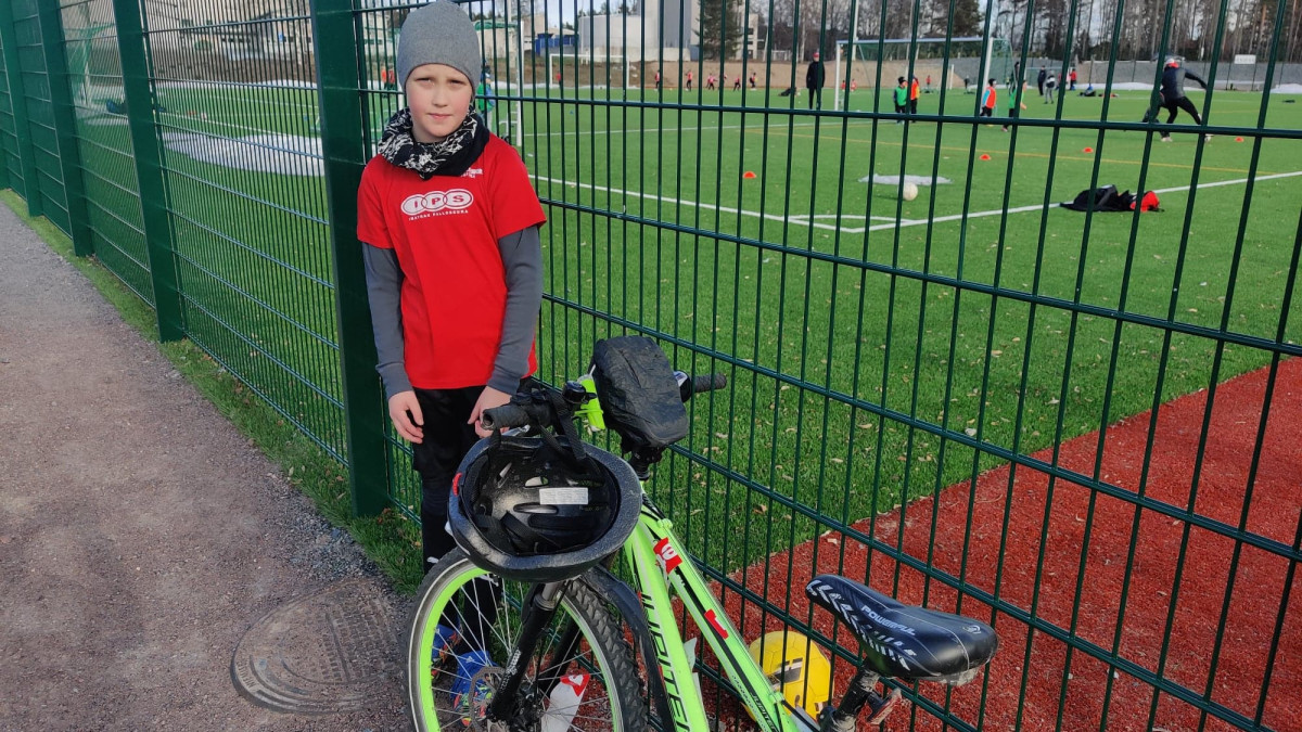 Poika ja polkupyörä jalkapallokentän laidalla.