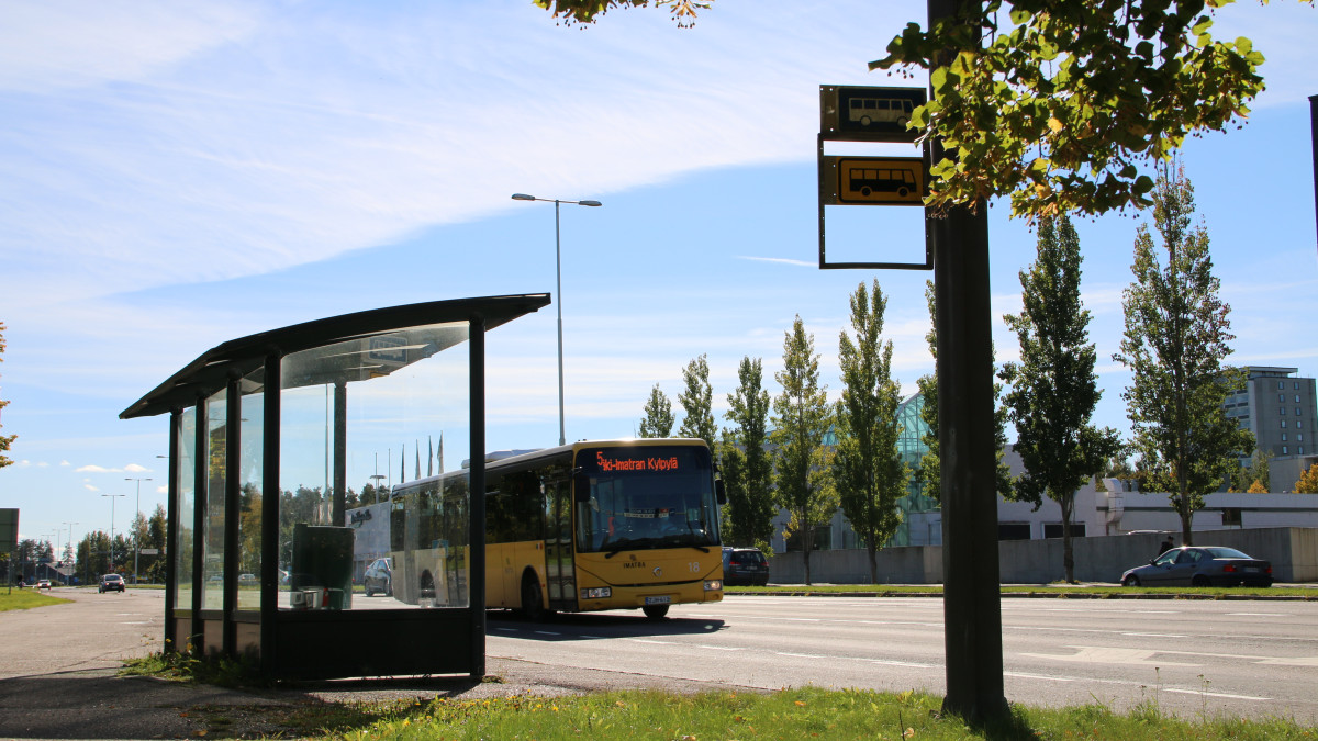 Автобус проезжает мимо автобусной остановки в солнечную погоду.