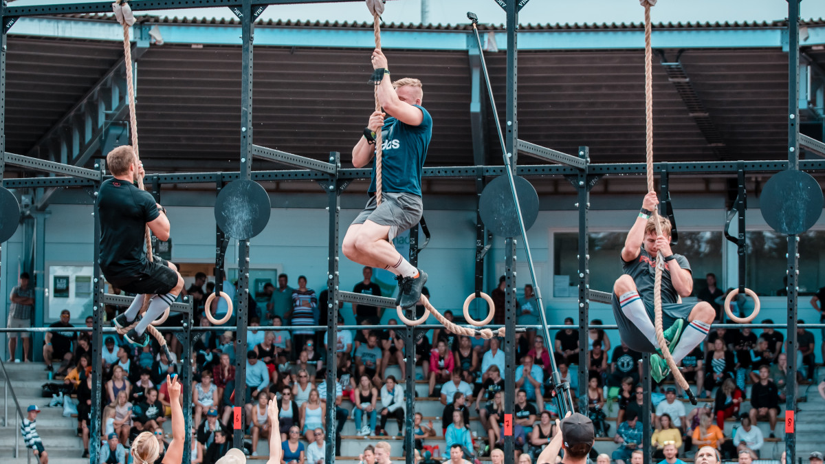 CrossFit kilpailu. Osallistujat kiipeävät köyttä pitkin ylös. Yleisöä taustalla.