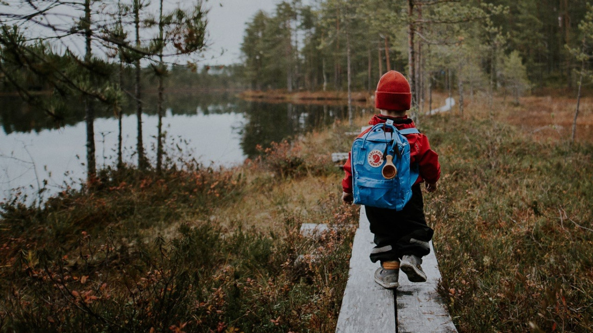 Lapsi kävelee pitkospuita pitkin reppu selässä suon reunalla syksyllä, VisitFinland.