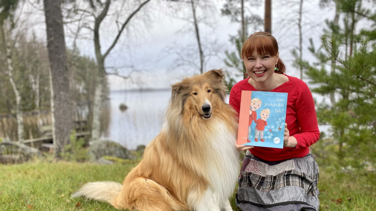 Koira ja nainen, joka pitelee lastenkirjaa.