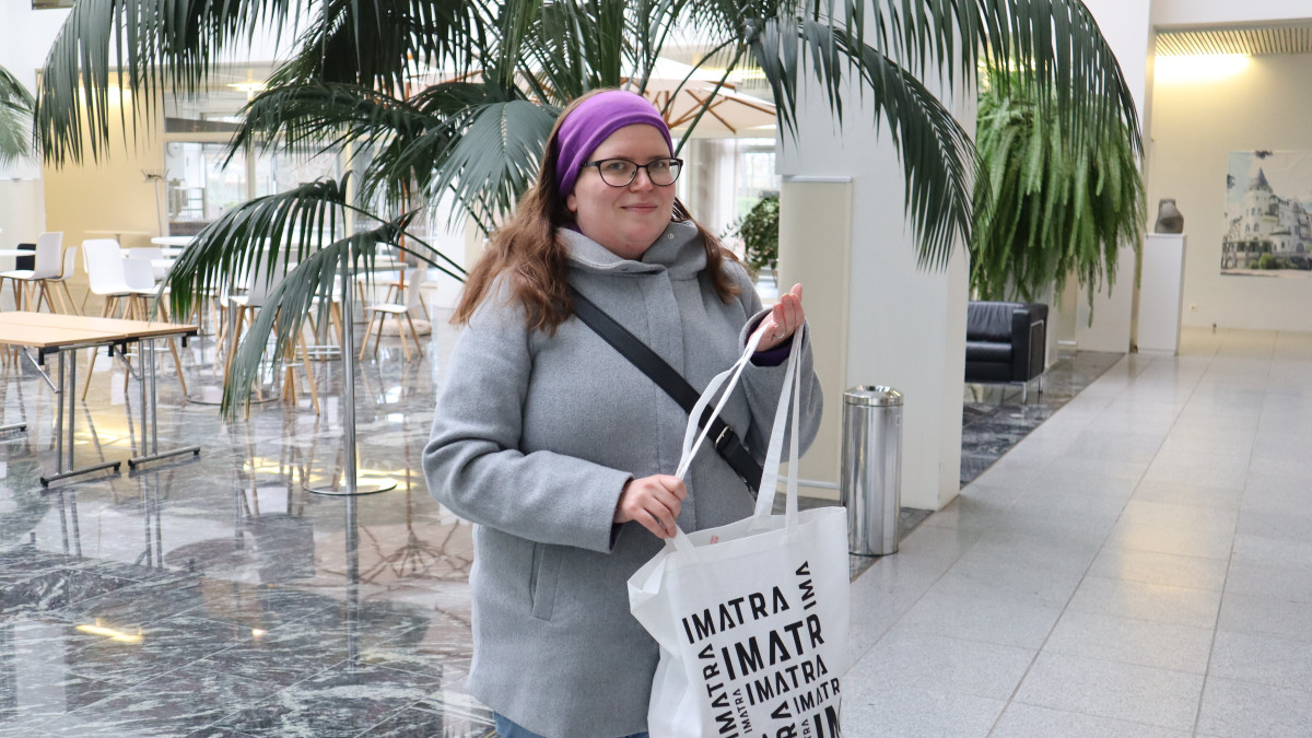 Jenni Könönen kaupungintalon aulassa Imatra-tuotekassi kädessään.