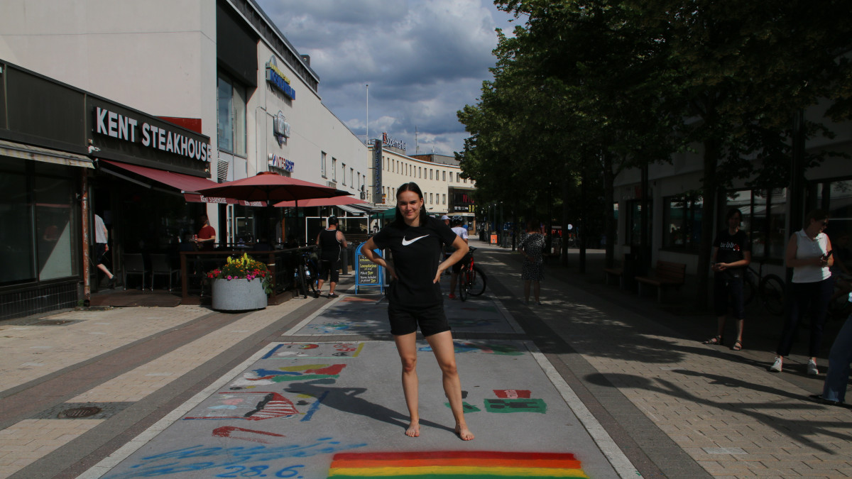 Salminen stands behind the pride flag he painted, with a pedestrian street in the background.