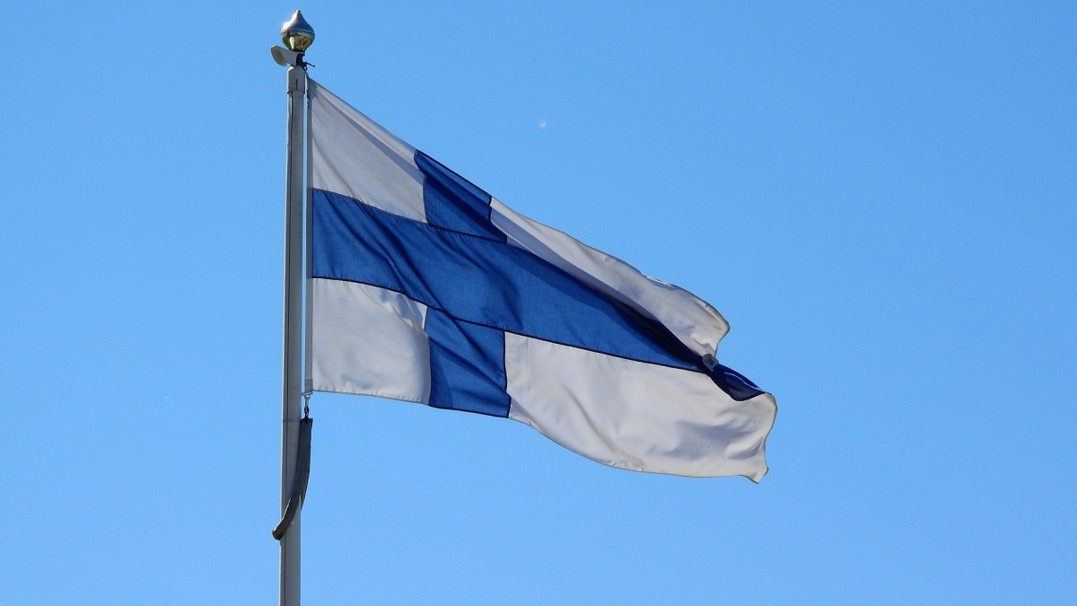 Suomen lippu heiluu tuulessa sinistä taivasta vasten.