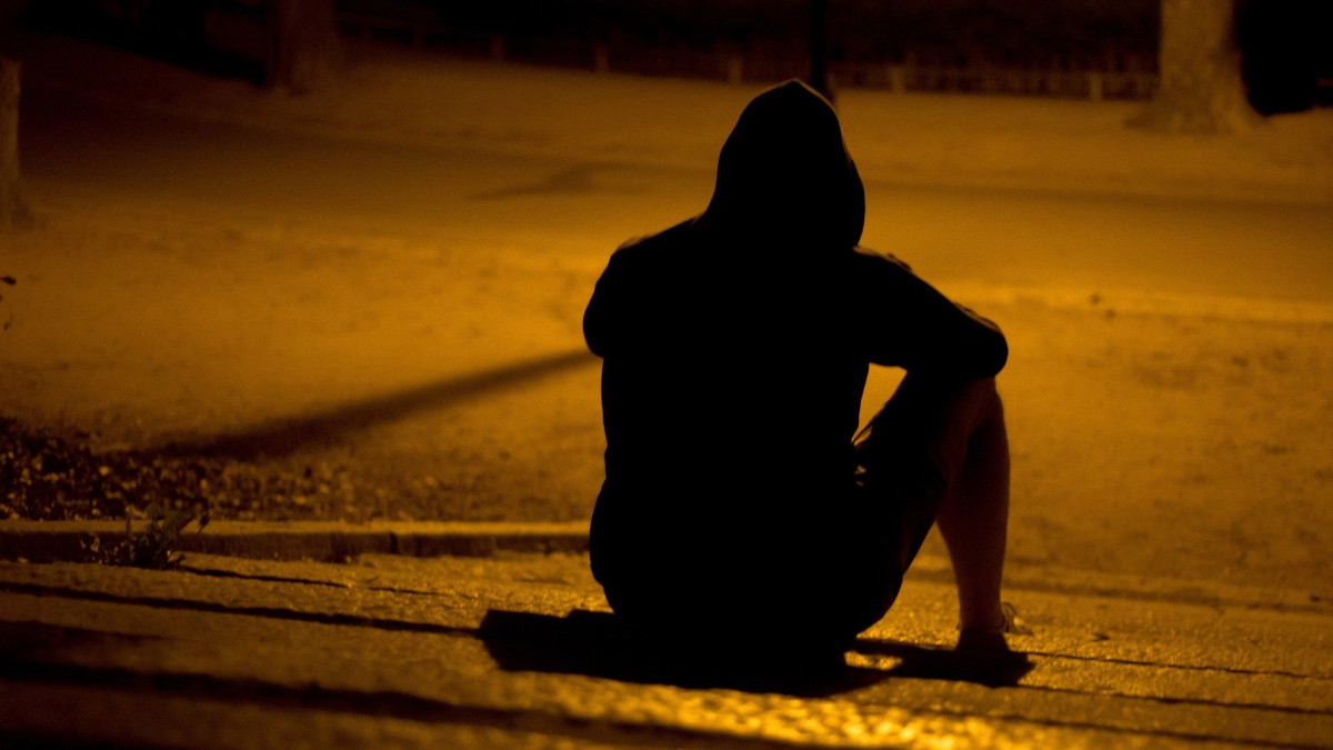 A young man sits on a dark street.
