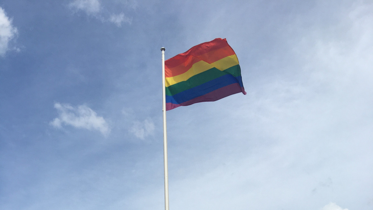The rainbow flag flies on the flagpole of the Ukonniemi sports field. The sky and a few clouds in the background.