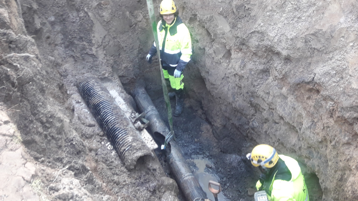 двое мужчин ремонтируют водопровод в яме.