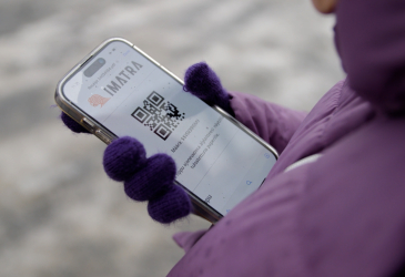 Lilatakkisella henkilöllä kädessään kännykkä, jonka ruudulla Imatran logo ja QR-koodi.