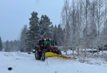 Traktori auraa jalkakäytävää lumisateessa.