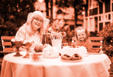 Vanha nainen ja pikkutyttö hymyilevät pitopöydän ääressä.