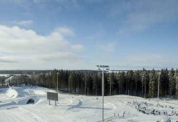 Ilmakuva Ukonniemi-stadionilta talvella. Etuosassa latuja, taustalla metsää ja sininen, aurinkoinen taivas.