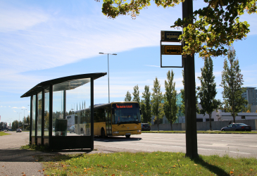 A bus drives past a bus stop in sunny weather.