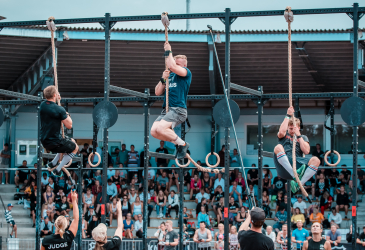 CrossFit competition. The participants climb up along the rope. Audience in the background.