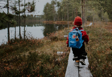 A child walks along the tall trees with a backpack on the edge of a bog in autumn, VisitFinland.