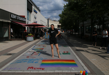 Салминен стоит за нарисованным им флагом гордости на фоне пешеходной улицы.