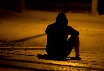 Nuori mies istuu pimeällä kadulla.
