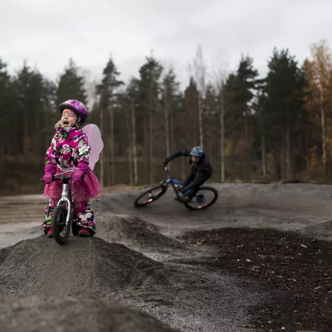 A child dressed in a red top is cycling with a helmet on the pump track.