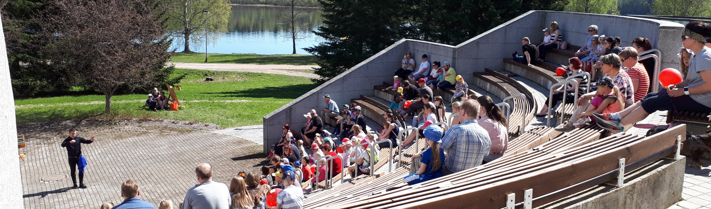 Yleisö seuraa kesällä ulkokatsomossa Vuoksen varrella esitystä.