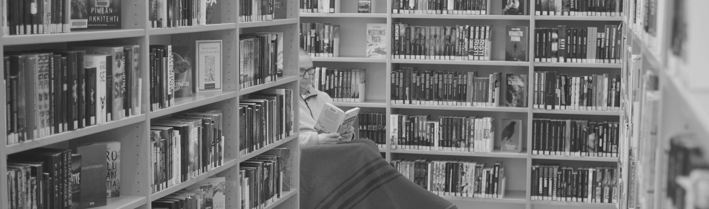 A man sits reading surrounded by bookshelves.