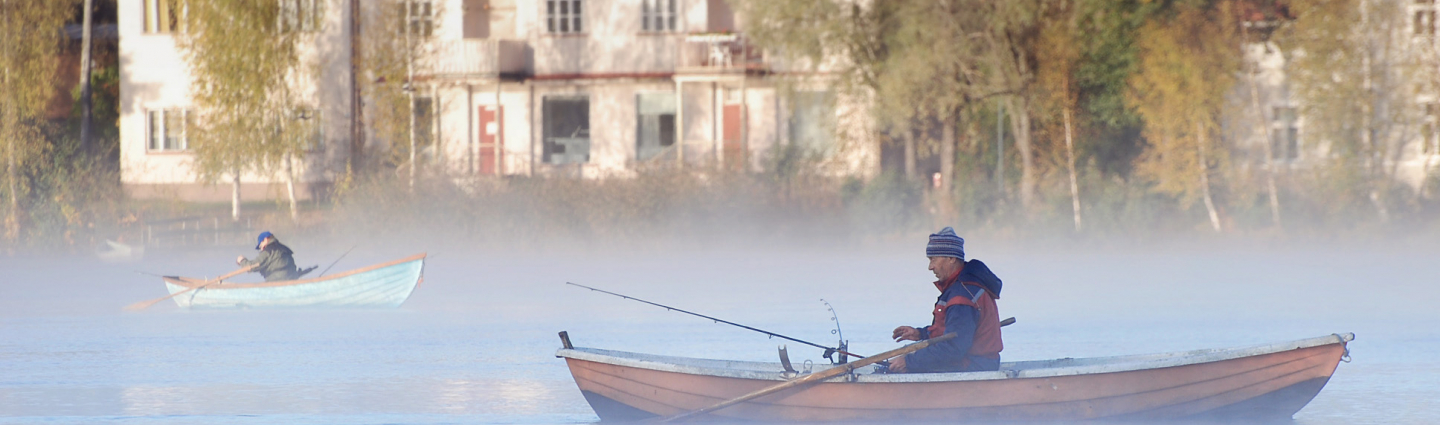 A fisherman in a rowing boat, a small apartment building in the background.