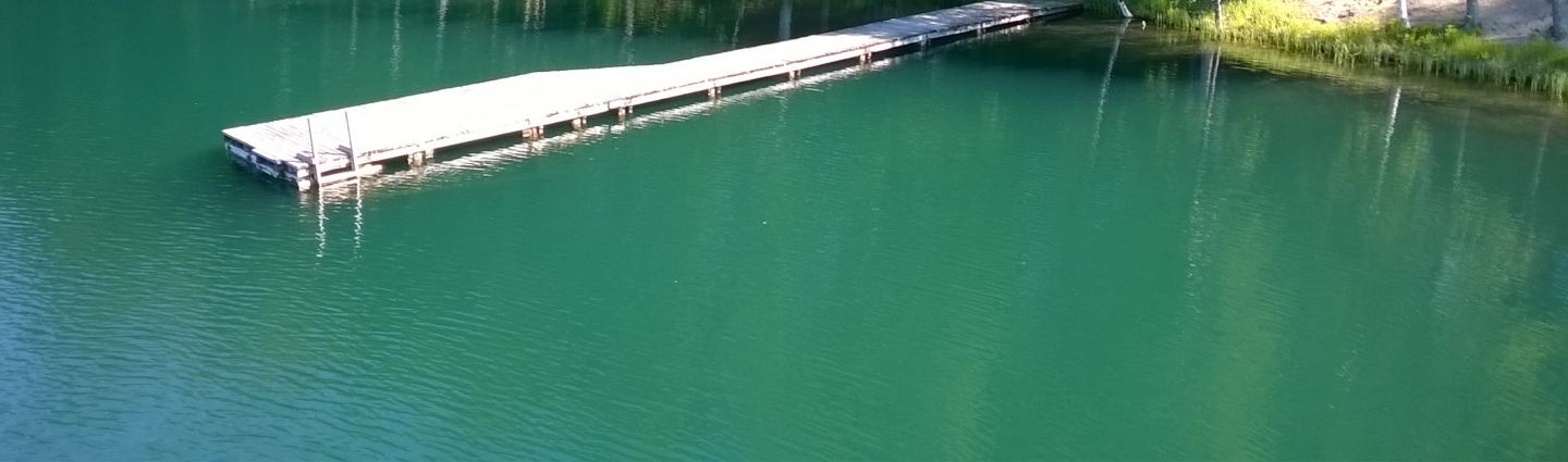 Näkymä uimarannalta, laituri ja vihreäsävyistä vettä.