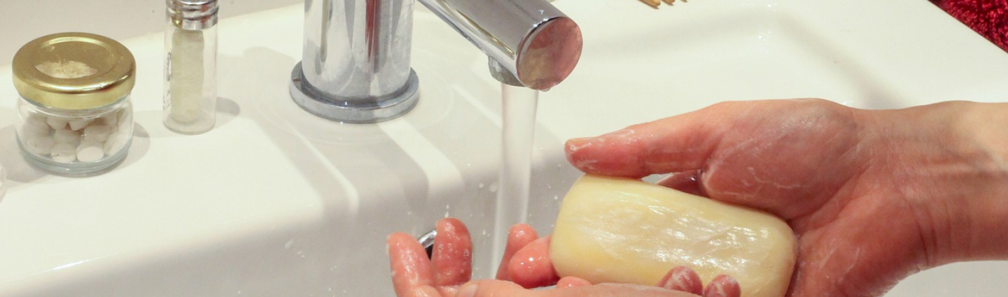 Henkilö pesee käsiä valuvan hanan alla. Kädessä palasaippua.