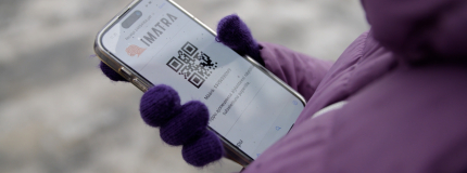 The person in the purple jacket is holding a mobile phone with the Imatra logo and QR code on the screen.
