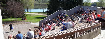 Yleisö seuraa kesällä ulkokatsomossa Vuoksen varrella esitystä.