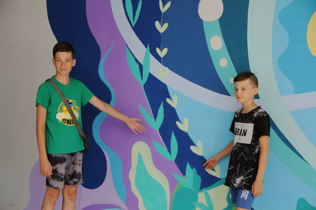 Kaksi poikaa seinämaalauksen edessä näyttämässä maalaamiaan kohtia.