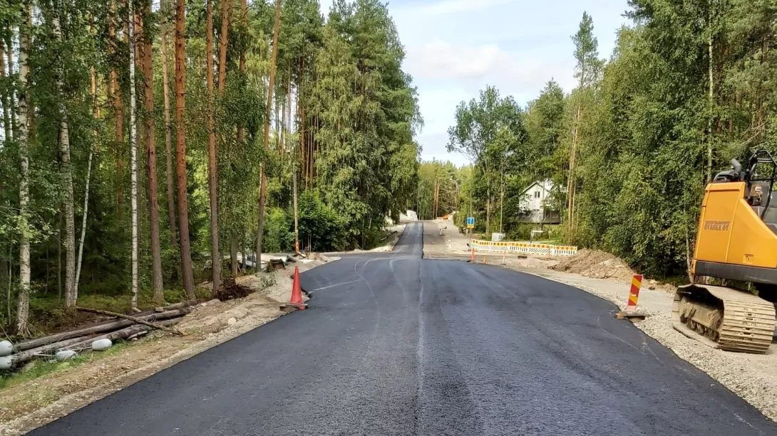 Uutta asfalttipintaa kadulla, ympärillä metsää, tien vieressä kaivinkone.