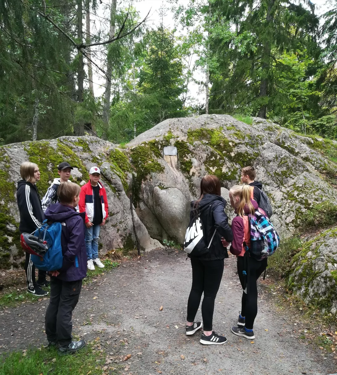 Yläkoulun oppilaat luonnossa. Taustalla iso kivi.